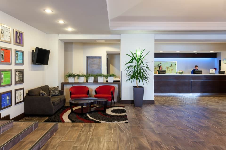 Contemporary hotel lobby featuring red accent chairs, dark wood flooring, artwork, and reception desk