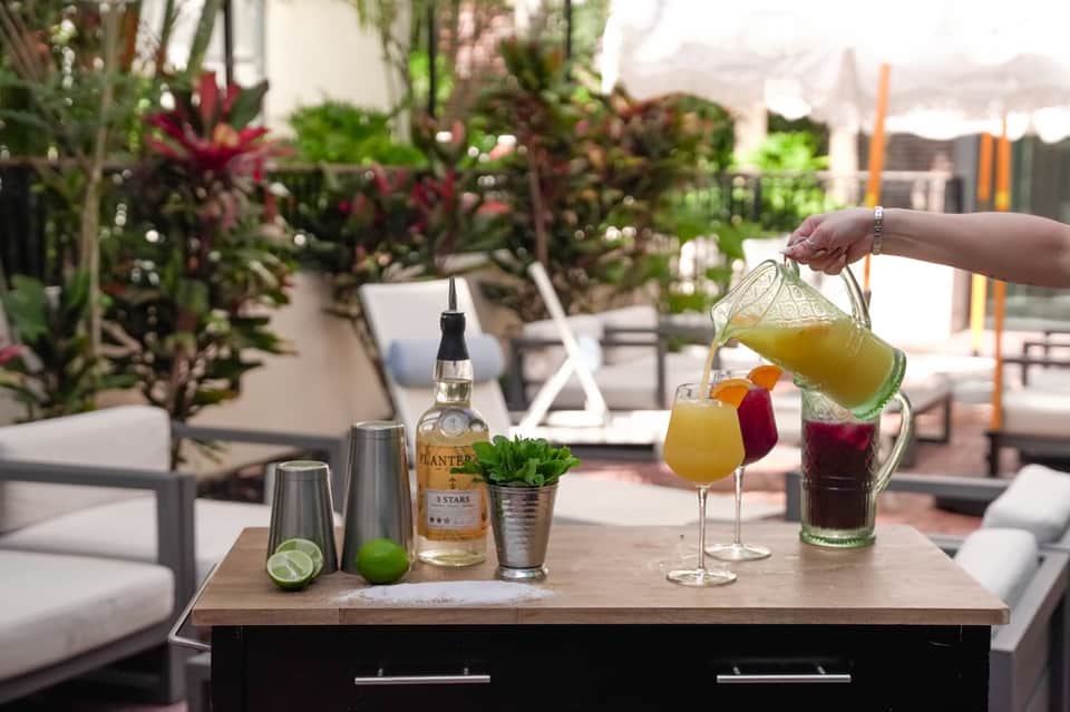 Rooftop bar service with colorful cocktails, tropical plants, and lounge seating at sunset