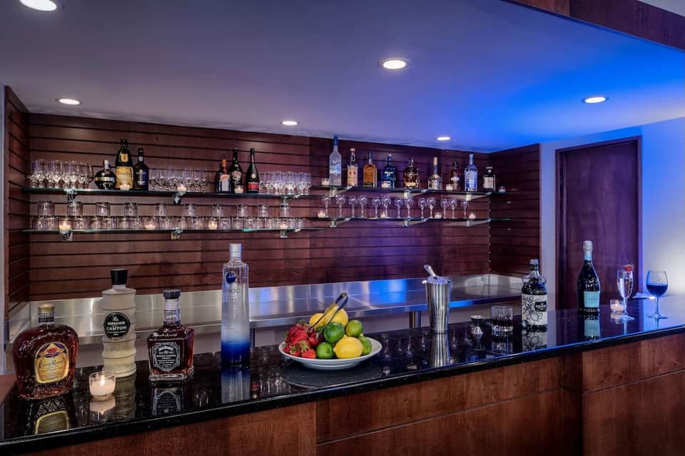 Upscale bar with wood-paneled walls, extensive liquor selection, blue accent lighting, and black countertop
