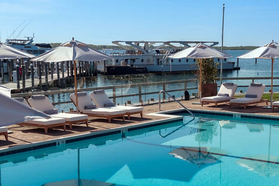 Waterfront resort pool deck with lounge chairs, umbrellas, and boats docked in turquoise water