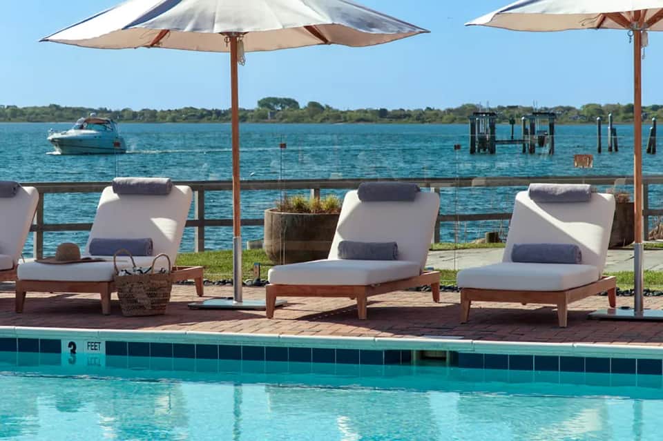 Waterfront pool lounge with white umbrellas, lounge chairs, and bay views