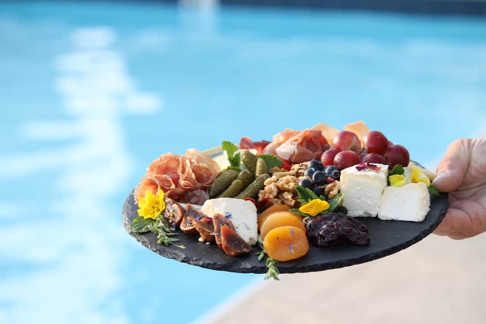 Gourmet charcuterie board with cured meats, cheeses, fruits, and edible flowers by poolside