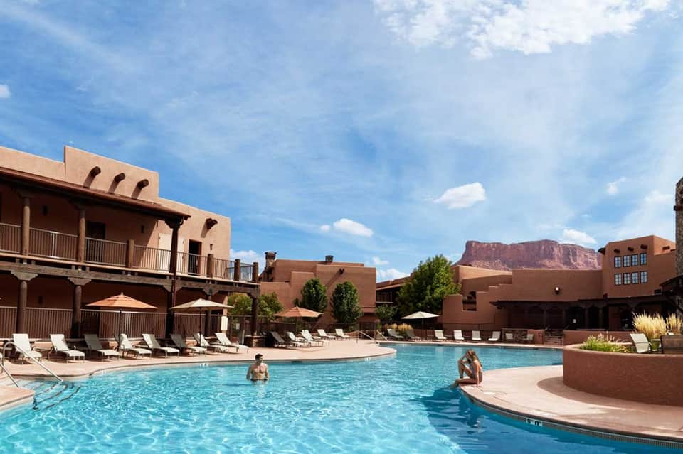 Resort pool with Southwestern architecture, white lounge chairs, and red rock mountain view