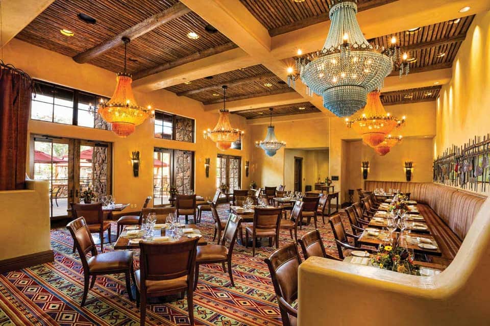 Elegant dining room with golden walls, decorative chandeliers, and formally set tables