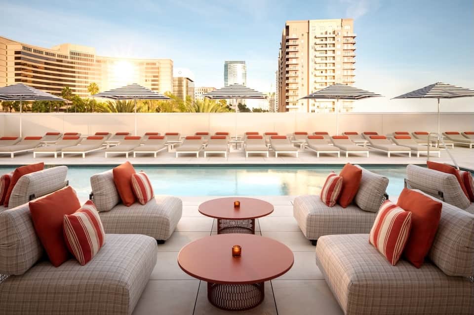 Resort pool deck with red and white lounge seating, umbrellas, and city skyline view