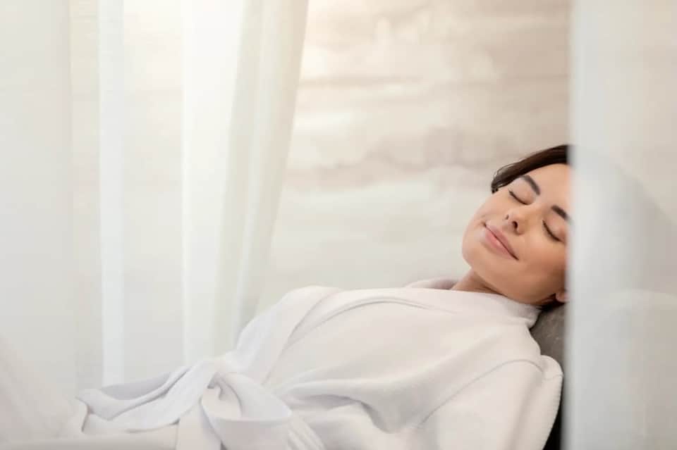 Woman peacefully resting on white bedding in serene, minimalist bedroom setting