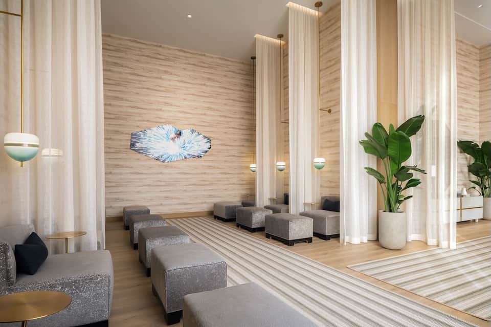 Spa relaxation area with wooden walls, tall sheer curtains, natural light, and lounge seating