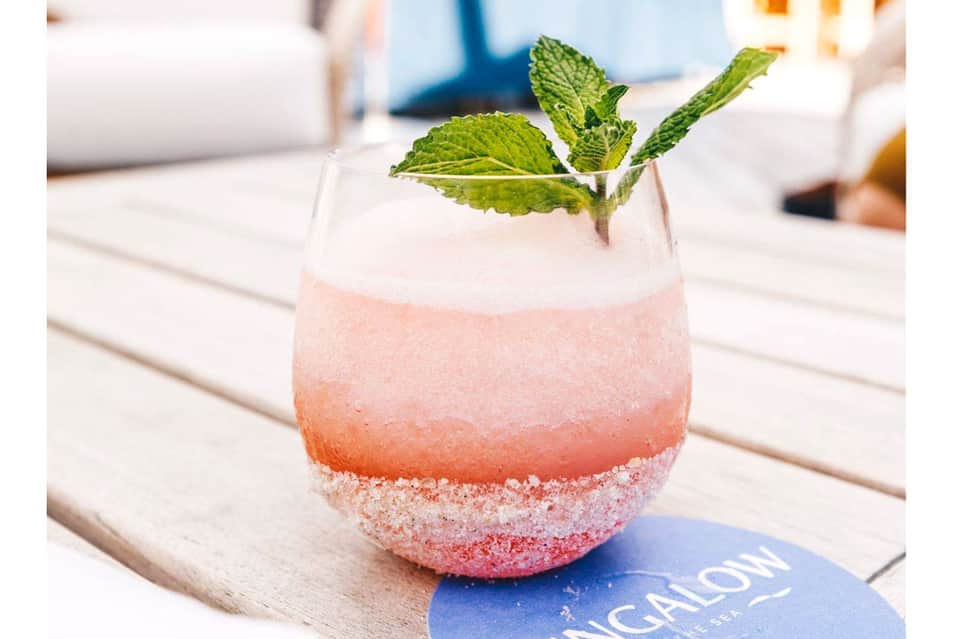 Colorful pink cocktail with mint garnish and sugar rim on wooden poolside table