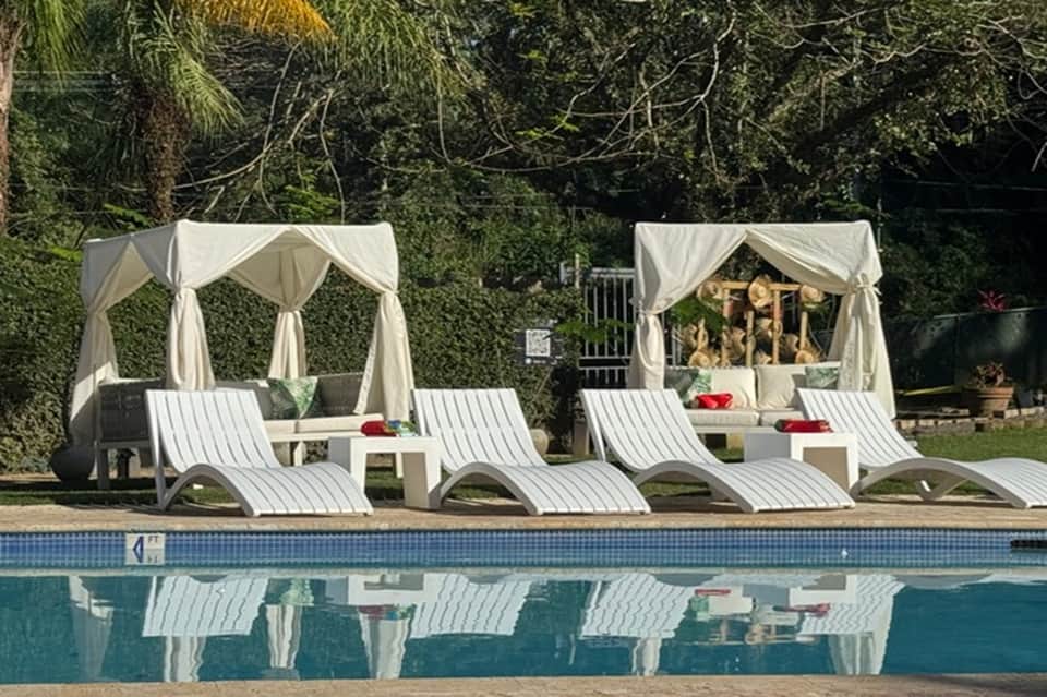 Poolside cabanas with white curtains, lounge chairs, and spa treatment beds near swimming pool