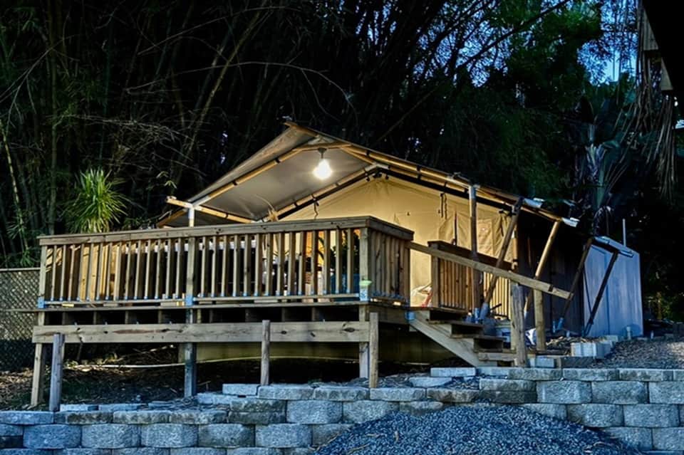 Illuminated glamping tent on elevated deck with tropical surroundings