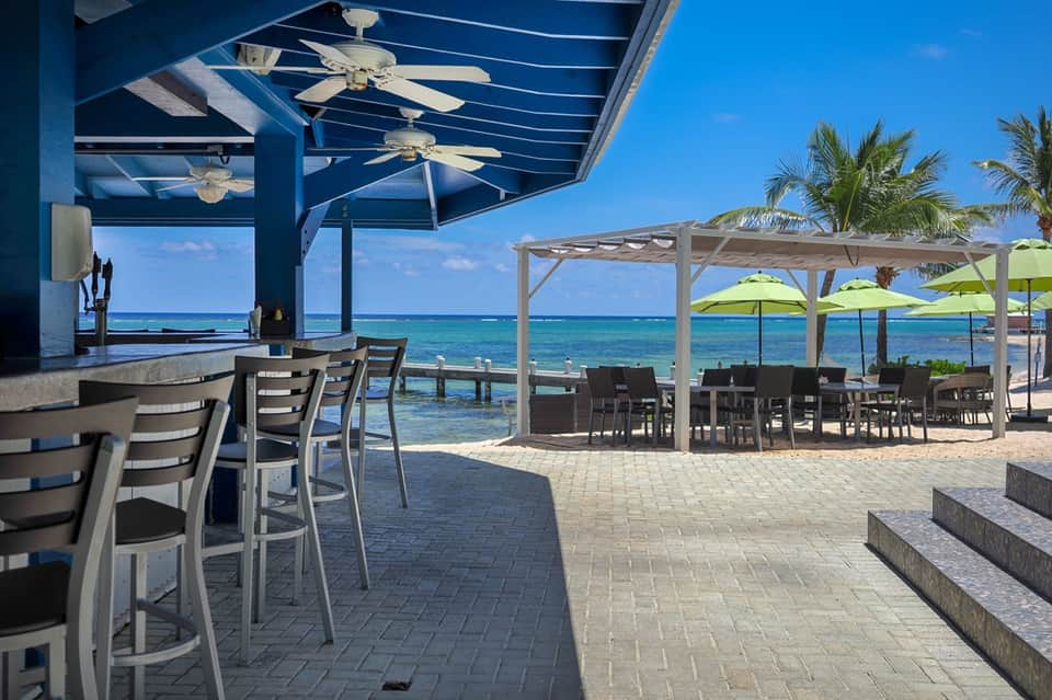 Beachfront bar and dining area with blue pergola, turquoise umbrellas, and ocean view