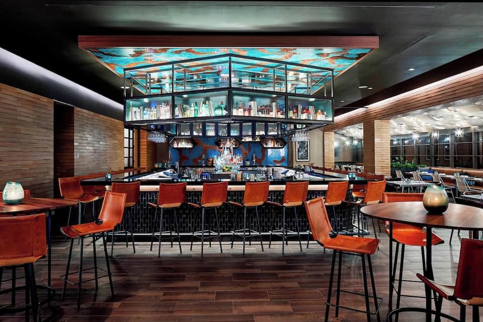 Modern hotel bar lounge with red leather seating, turquoise ceiling art, and multiple levels