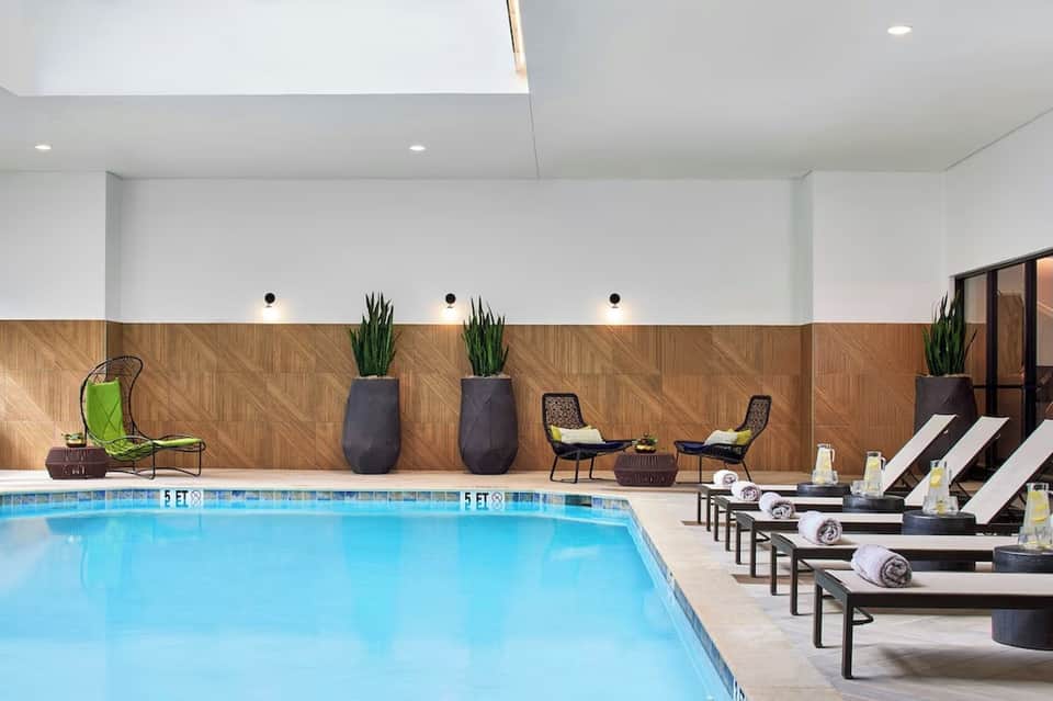 Indoor pool facility with modern design, lounge chairs, potted plants, and recessed lighting