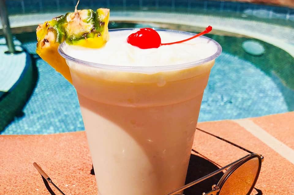 Creamy tropical drink with pineapple garnish and cherry at pool edge