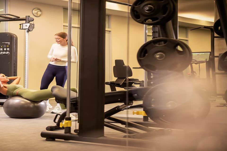 Female fitness instructor demonstrating exercise beside equipment in modern gym