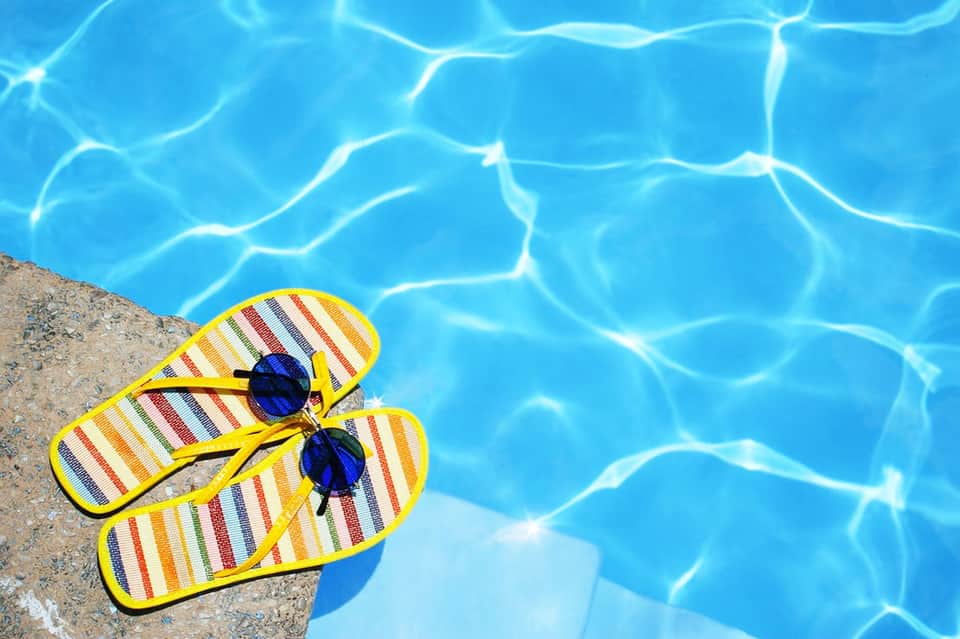 Yellow striped flip-flops and sunglasses resting on pool edge with crystal-clear blue water