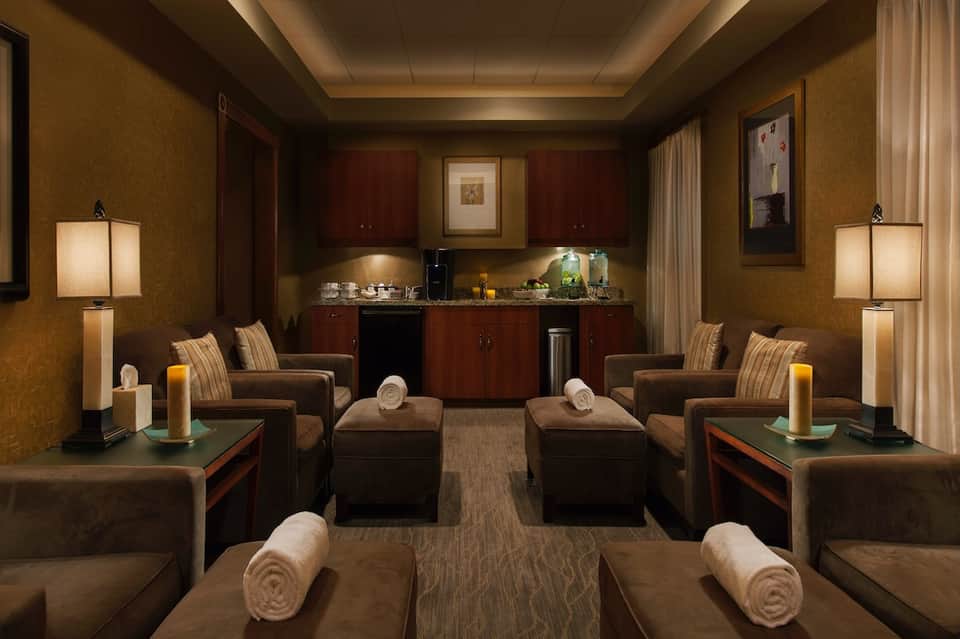 Luxury spa relaxation room with brown leather recliners, dim lighting, and beverage station