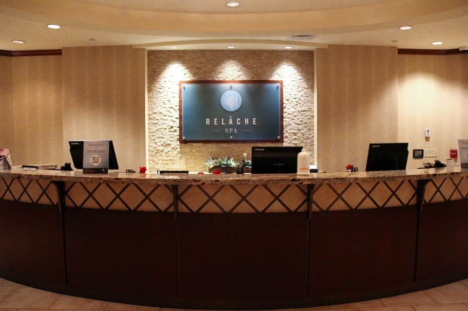 Spa reception desk with stone accent wall, curved counter, dark wood paneling, and Relâche Spa branding