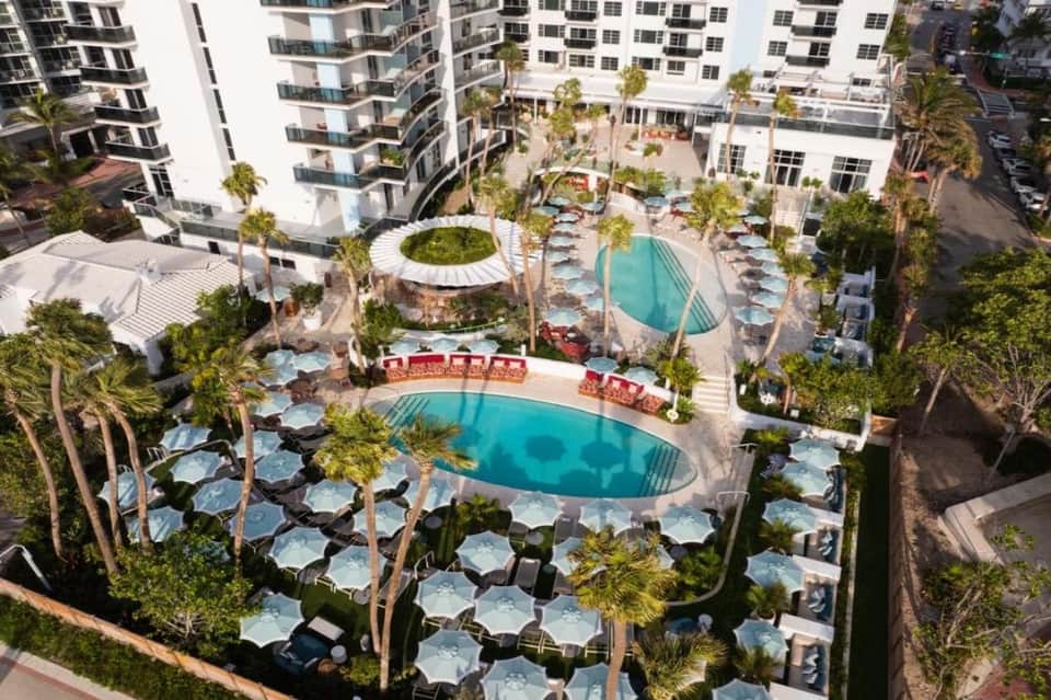 Aerial view of resort complex with two curved pools, lounge chairs, and surrounding hotel buildings