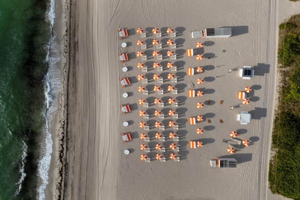 Aerial view of beach with organized orange and white umbrellas and sunbeds