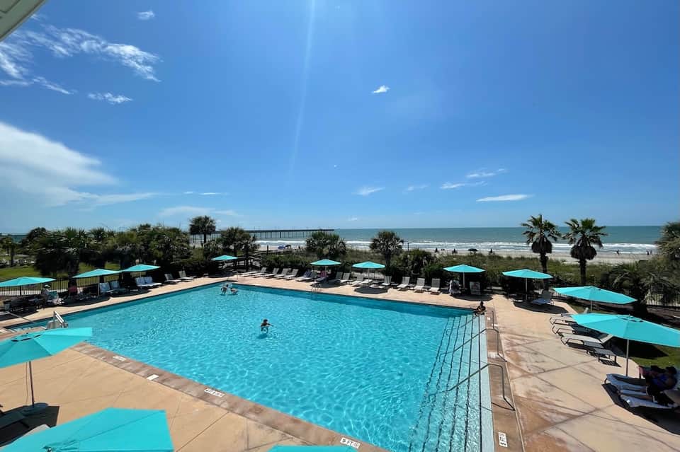 Oceanfront swimming pool with turquoise water, lounge chairs, umbrellas, and beach access