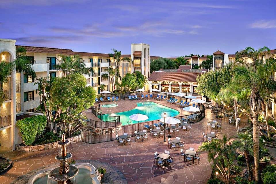 Expansive resort courtyard with curved pool, palm trees, and multi-story hotel buildings at dusk
