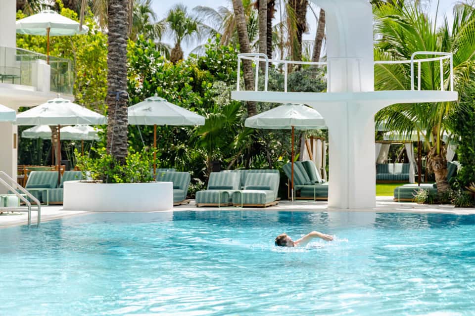 Contemporary pool with striped lounge chairs, umbrellas, white column, and palm trees