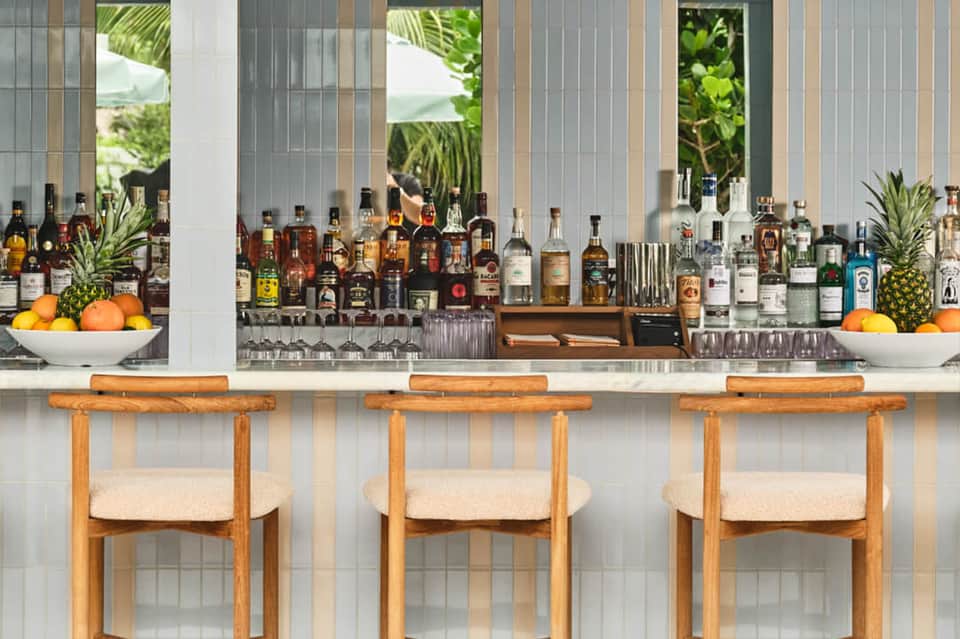 Tropical beach bar with wooden stools, spirits bottles, and palm tree views