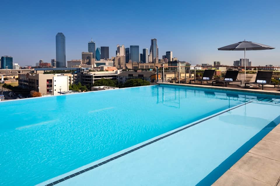 Urban rooftop infinity pool with Dallas skyline backdrop and modern sun loungers