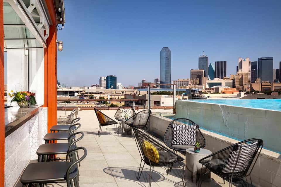 Rooftop bar and pool deck with city skyline views, modern seating, and blue pool
