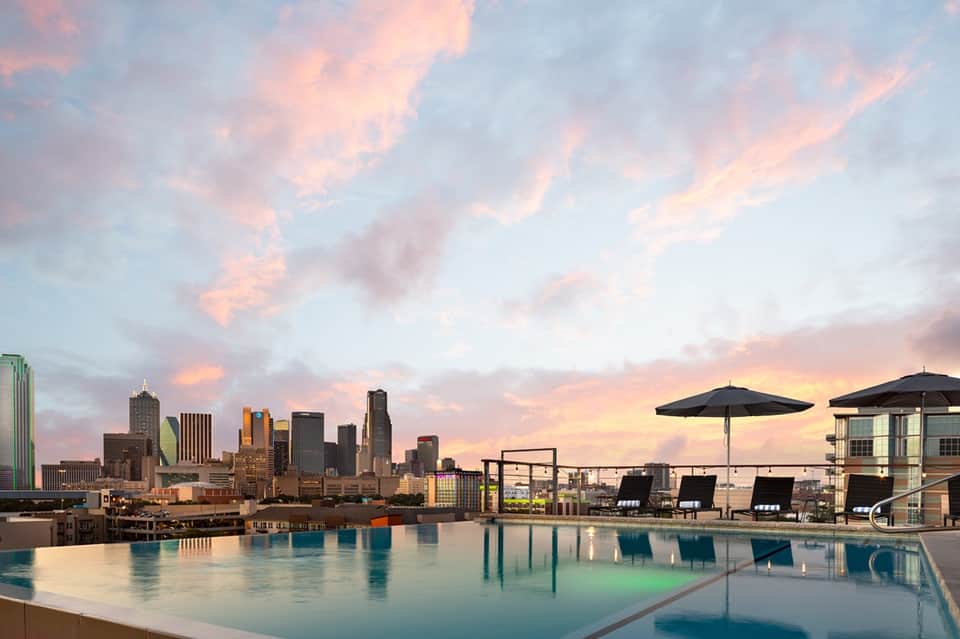 Rooftop infinity pool with city skyline view at dusk with umbrellas and lounge chairs