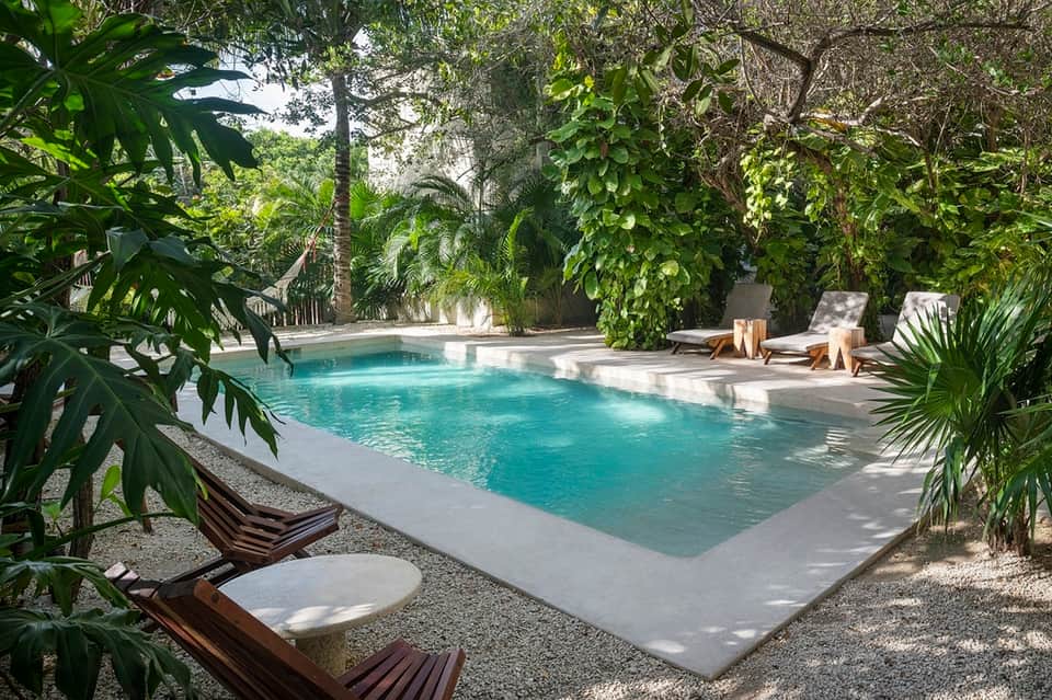 Tranquil resort pool surrounded by lush tropical vegetation and wooden lounge chairs with cushions