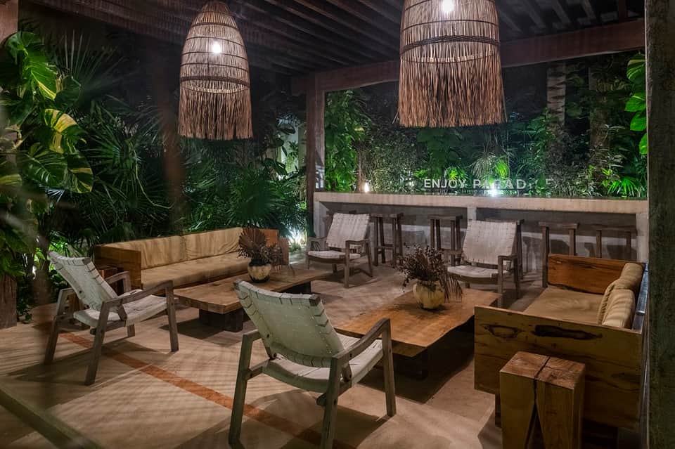 Indoor tropical lounge with woven pendant lights, lush green plants, wooden furniture, and ambient lighting