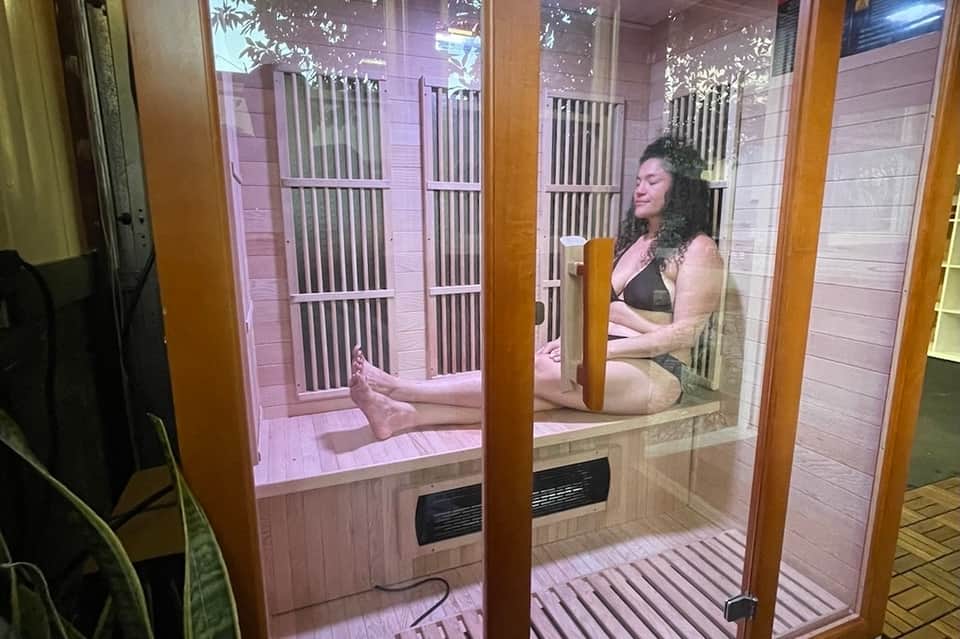 Infrared sauna interior with woman sitting on wooden bench, glass door, and purple lighting