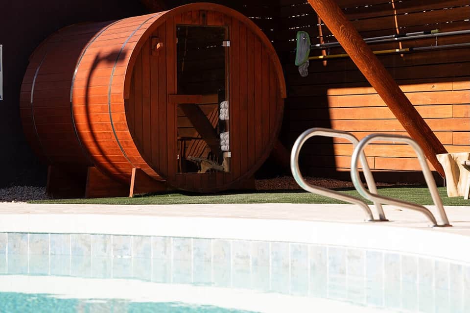 Wooden sauna barrel beside an outdoor pool with modern architecture