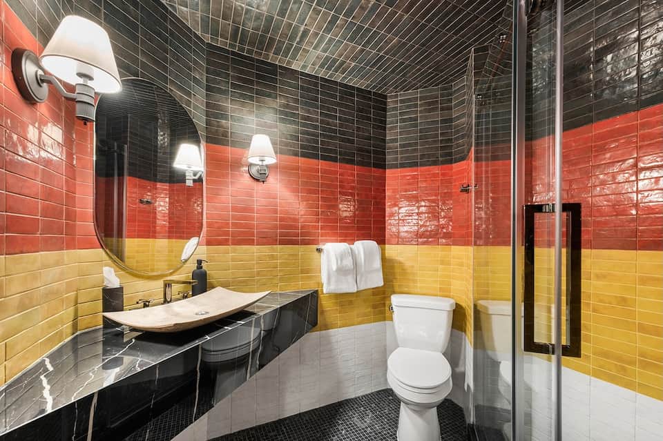 Modern bathroom with black and yellow tile work, round mirror, vessel sink, and glass shower enclosure