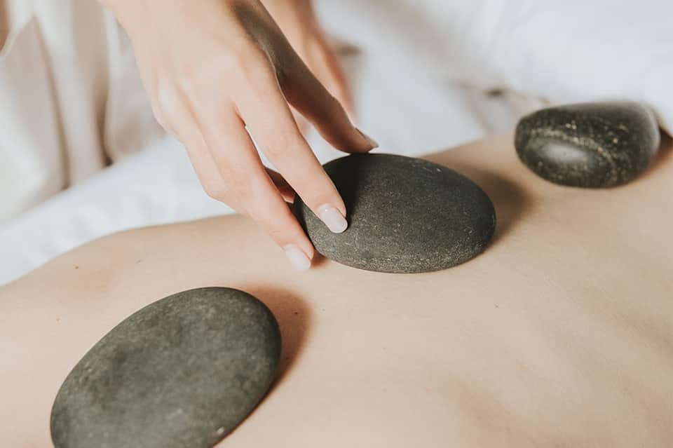 Close-up of hot stone massage therapy with person's hands placing smooth basalt stones on client's back