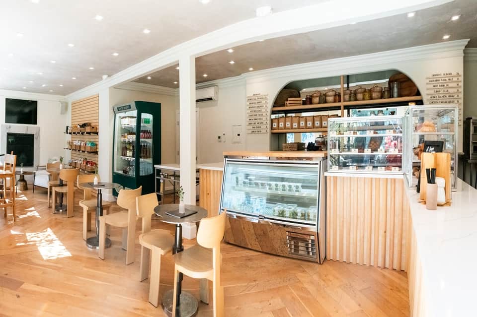 Bright café interior with wooden furniture, refrigerated display case, and open shelving
