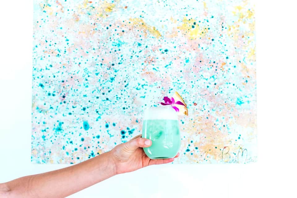 Hand holding mint green ceramic mug with colorful speckled background