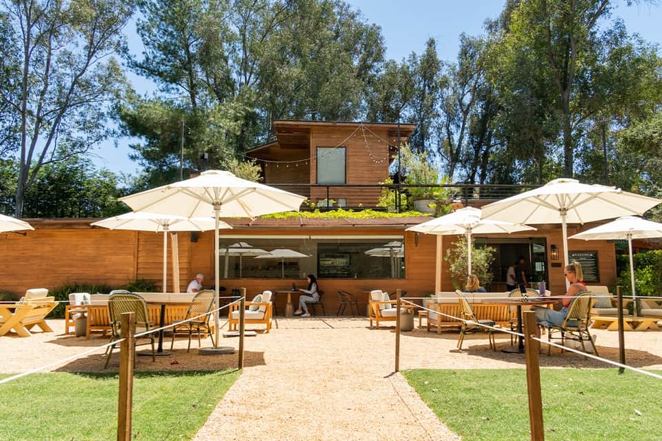 Contemporary resort outdoor patio with cream umbrellas, wooden furniture, and tree-lined setting