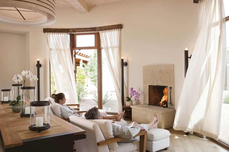 Spa relaxation room with fireplace, cream seating, flowing white curtains, and ocean view doors