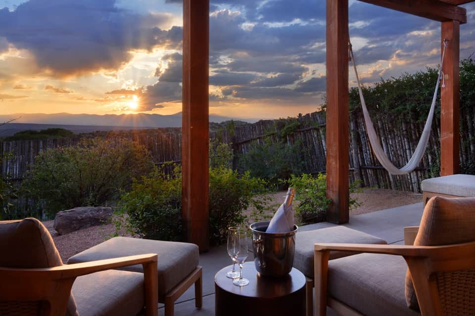 Desert sunset view from covered patio with wooden posts, comfortable seating, and wine service