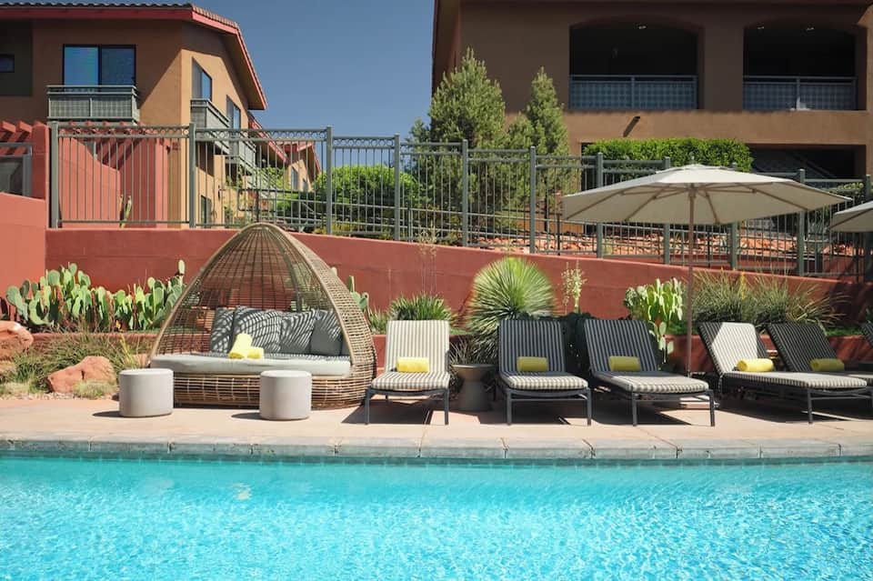 Resort pool area with lounge chairs, umbrella, woven sunbed, desert landscaping, and terracotta architecture