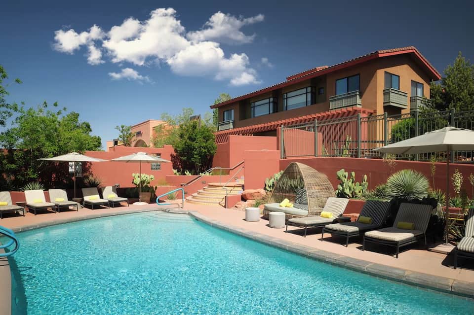 Resort courtyard with turquoise swimming pool, lounge chairs, and red-toned buildings