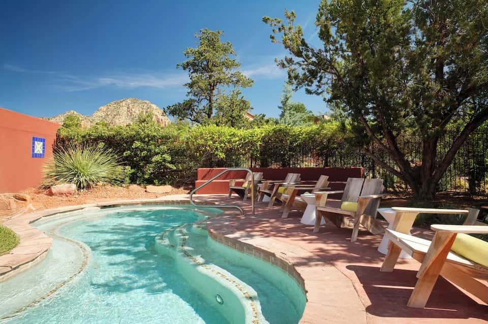 Desert resort pool with turquoise water, lounge chairs under trees, and red accent wall