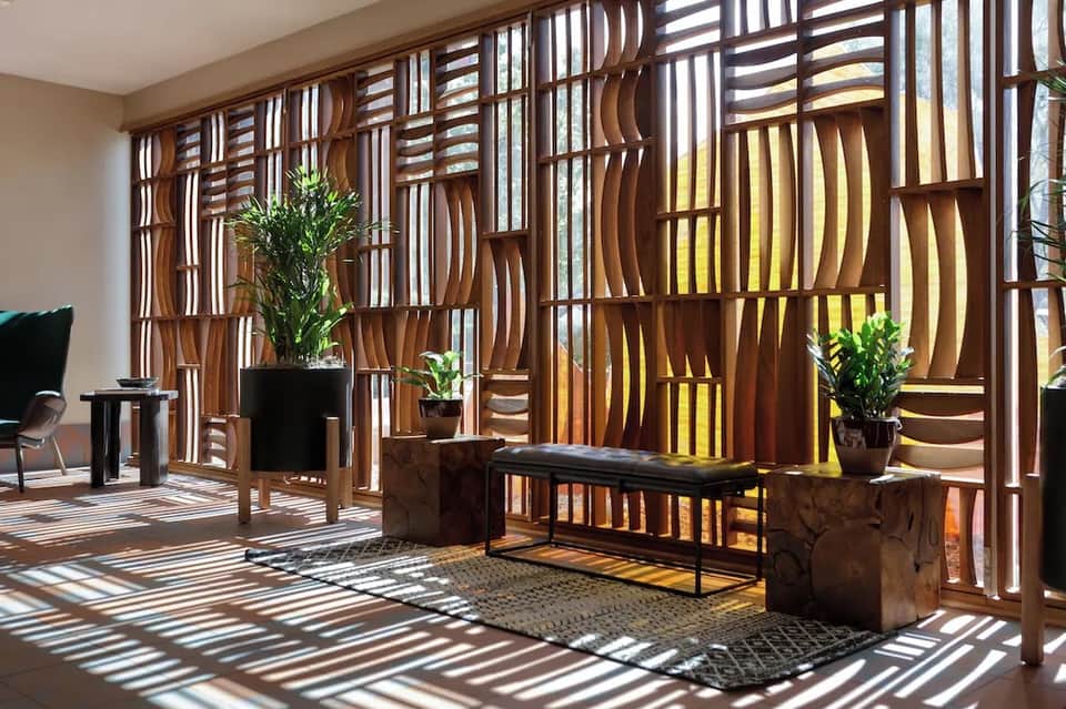 Modern lobby with wooden geometric screen wall, natural light, potted plants, and black furniture