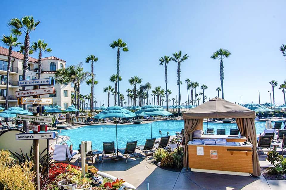 Beachfront resort pool with turquoise water, palm trees, and blue umbrellas under clear sky