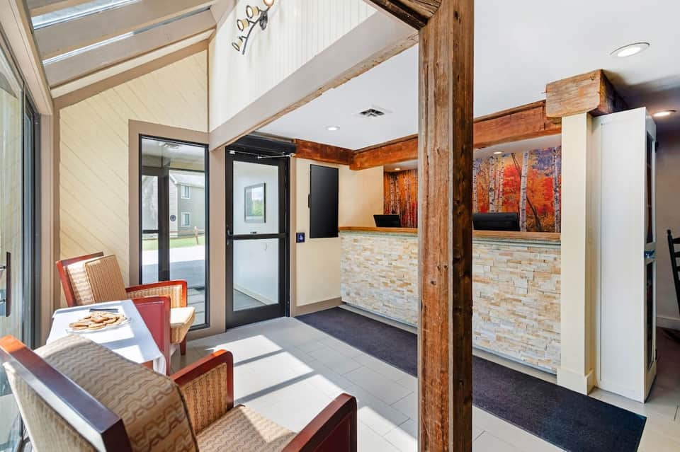 Modern hotel lobby with vaulted ceiling, exposed wooden beams, stone accent wall, and contemporary seating