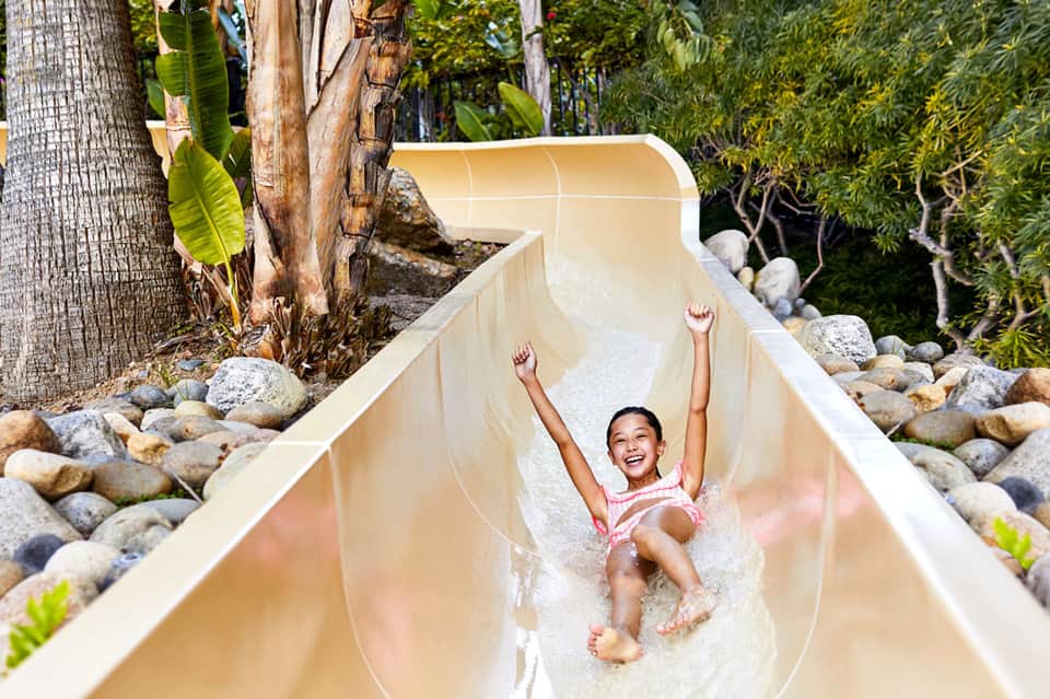 Child sliding down a white water slide surrounded by tropical vegetation and palm trees