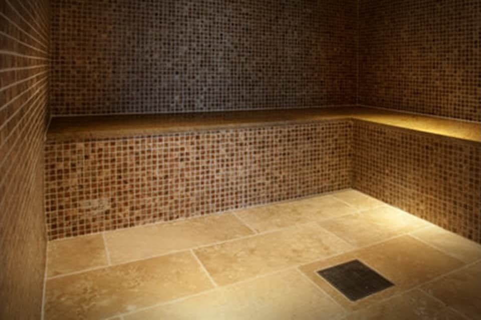 Spa steam room with mosaic tile walls and heated bench seating